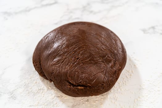 Overhead view of unwrapped chocolate cookie dough shaped into a smooth ball on a lightly floured marble surface.