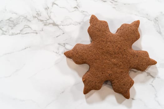 Overhead view of a single Chocolate Ginger Sugar Cookie in a snowflake shape placed on a marble surface, showcasing its crisp edges and deep chocolate color.