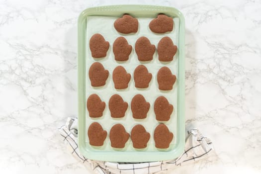 Overhead view of mitten-shaped Pale Gingerbread Cookies freshly baked on a tray, cooling on parchment paper.