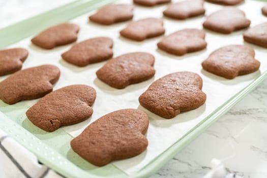 Front-facing view of freshly baked Pale Gingerbread Cookies in mitten shapes resting on a parchment-lined tray, just out of the oven.