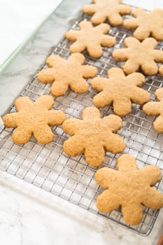 Angled top view of amber gingerbread cookies in snowflake shapes cooling on a wire rack, showcasing their golden-brown texture and festive design.