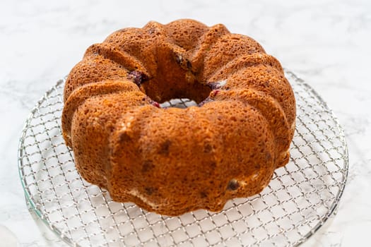With precision, the bundt cake is carefully removed from the pan - placed onto a round cooling rack, preparing it for a flawless presentation and delightful indulgence.