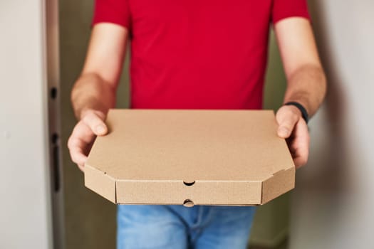 delivery man in red t-shirt giving food order and holding pizza box at home, close-up