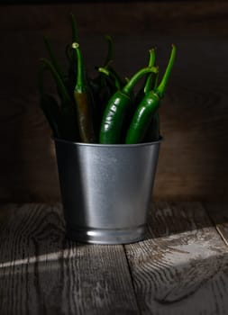 Bright green chilies in a metallic pot enhance the rustic charm of the wooden setting and soft lighting.