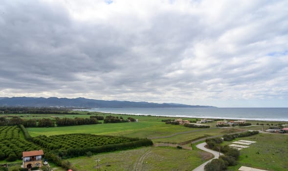 Rolling green fields meet the coastline under a vast sky with soft clouds, creating a tranquil scene.