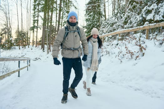 This high-resolution photograph captures a heartwarming scene of a family walking through a snowy forest in winter. The family, consisting of a man, woman, and boy, is enjoying the serene and picturesque landscape as they stroll along the icy path. The candid moment is beautifully captured in portrait mode, highlighting the joy and togetherness of the family. The snowy forest provides a stunning backdrop, with the crisp white snow contrasting against the lush evergreen trees. This image is perfect for themes related to family, winter travel, nature, and scenic landscapes, offering a detailed and evocative representation of a winter wonderland. Family walking through a snowy forest in winter, with a man, woman, and boy enjoying the scenic landscape, capturing a candid moment in high-resolution photography.
