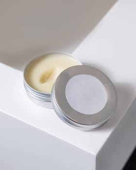 Opened body butter jar with blank label on round lid on white washbasin in bathroom, close up. Natural herbal cosmetic product for body care, daily routine or spa procedures