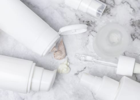 White opened cream tubes, bottles and jars on white marble table top view, mockup. Beige scrub and cream squeezed on table. Natural products for daily face care, spa procedures