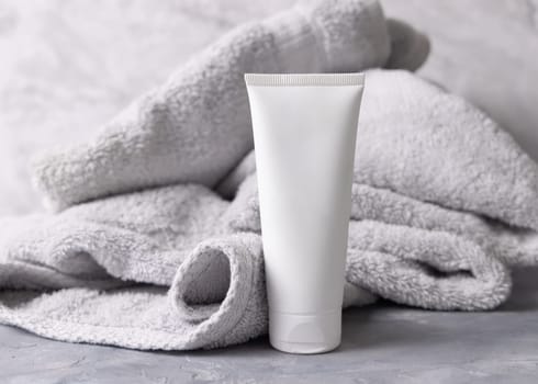 White blank cosmetic squeeze cream tube near light grey towel in bathroom top view, brand packaging mockup. Natural herbal cosmetic product for daily facecare, copy space