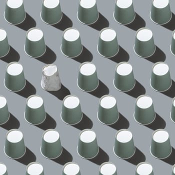 Disposable new light green paper cups and crumpled used white one in a line on gray top view, hard shadow, pattern, mockup with copy space. Empty cardboard coffee cups flat lay. Consumerism concept