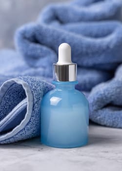 Glass dropper bottle with pipette near blue bath towel closeup, brand packaging mockup, copy space. Natural organic cosmetic product for facecare and spa procedures - serum or essence