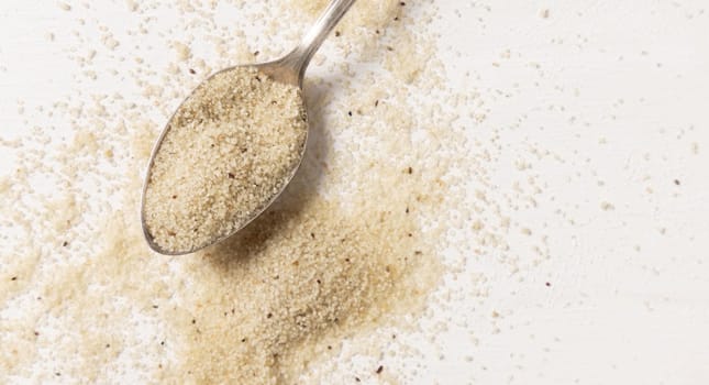 Raw uncooked fonio seeds in a metal spoon on white table top view, copy space. African ancient pseudocereal. Organic super food. Healthy food concept. Gluten free alternative seeds