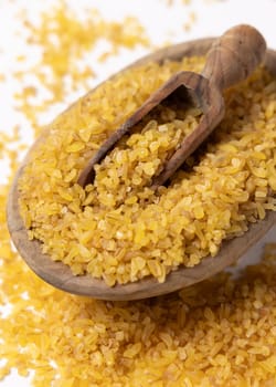 Raw dry uncooked yellow bulgur grain in a wooden spoon on a bowl on cream napkin closeup. Middle Eastern cousine. Organic super food for healthy diet. Ancient alternative cereal. seeds