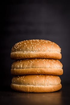 Empty burger bun with sesame seeds on a black table.