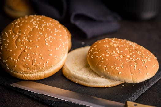 Empty burger bun with sesame seeds on a black table.