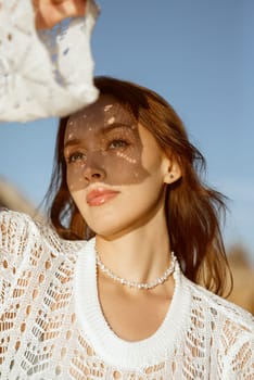 close-up of a beautiful young girl. she is looking at the sun. openwork shadow on her face. shadow of the lace sleeve of her dress. concept of a hot summer day.