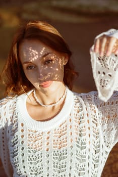 close-up of a beautiful young girl. she is looking at the sun. openwork shadow on her face. shadow of the lace sleeve of her dress, concept of a hot summer day