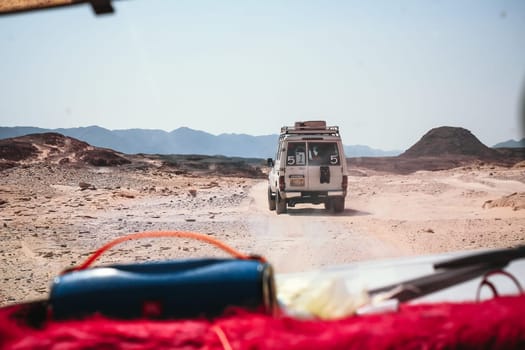 A jeep drives on a dusty desert road with its tires rolling on rough terrain, highlighting its rugged design and capability in this natural setting