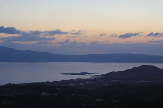 The Serene Twilight Casting Its Mystical Glow Over the Calm Sea and Rolling Hills. A beautifully tranquil sunset scene, showcasing serene calm waters reflecting the silhouettes of distant hills