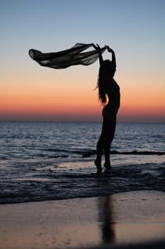 A girl on a beach in Greece during sunset standing on socks and holding a handkerchief in her hands