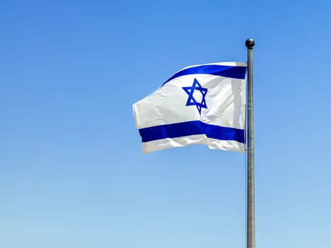 The Israeli flag waves in the bright sunlight, its blue Star of David prominent against the white background