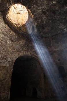 An ethereal cave scene where golden sunlight is streaming gracefully through a natural opening above