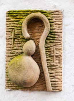 A weathered stone carving depicting a pilgrim's staff, embellished with symbols, along the Camino de Santiago.