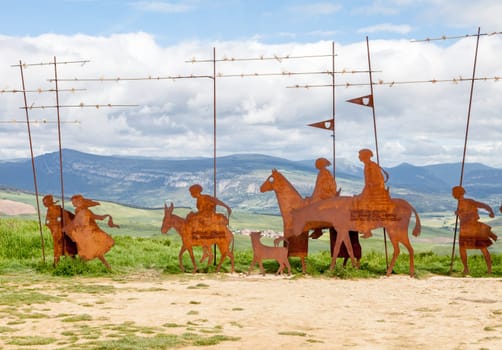 On the Camino de Santiago, metal sculptures of pilgrims walk toward stunning hills under a cloudy sky.