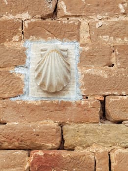 A shell symbol, representing pilgrimage, is affixed to a rustic brick wall along the Camino de Santiago.