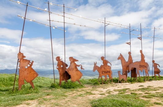 On the Camino de Santiago, metal sculptures of pilgrims walk toward stunning hills under a cloudy sky.