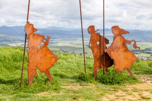 On the Camino de Santiago, metal sculptures of pilgrims walk toward stunning hills under a cloudy sky.
