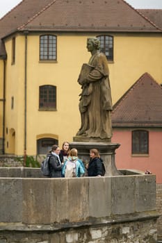 Wuerzburg, Germany – September 26, 2024: Figure of St. Totnan and some women at the tradition of drinking wine, Bruckenschoppen on the old Main Bridge in Wuerzburg