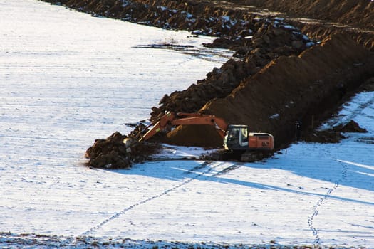Road construction. Excavator digs a trench for laying a sewer pipe on a cloudy winter day. Selective focus, shallow depth of field, engineering works