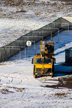 Mobile crane in a winter landscape, a large yellow crane with a long arm and attached basket against a clear blue sky, stationed on a snow-covered field