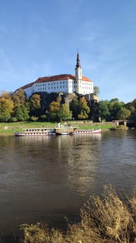 Castle riverside trees green nature summer autumn background landscape blue sky day. October 16 2024 Decin Czech Republic Europe travel places . High quality photo park outdoor historic buildings
