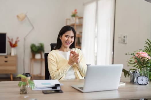 A delighted woman claps her hands in her home office, celebrating a recent accomplishment with enthusiasm and positivity.