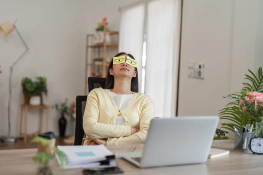 A woman wearing a sleep mask leans back in her chair at her home office, taking a break from work, embodying relaxation.