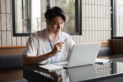 A young professional is focused on his laptop in a contemporary office setting, conducting online research and developing a project.