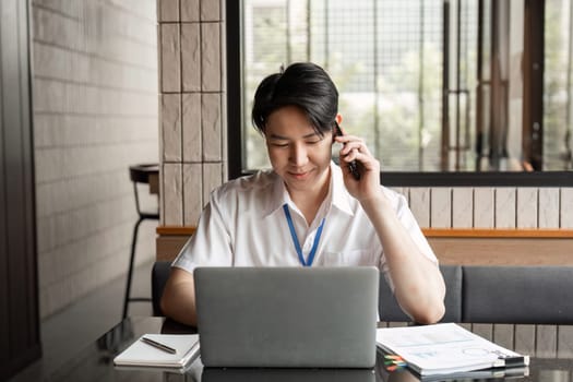 A young professional is engaged in a phone call while working on his laptop in a contemporary office, effectively balancing communication and project tasks.