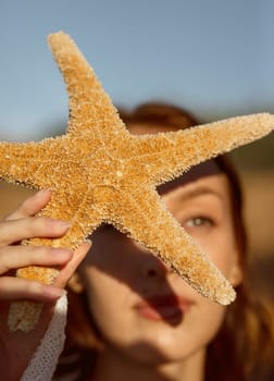 close up of beautiful young girl, starfish near her face, girl holding starfish near her face summer sea morning concept. focus on starfish