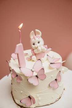White and pink cake with cute bunny for children's birthday . The cake is decorated with a cute bunny made of light icing. For a 1 year birthday for a little girl. There are pink butterflies on the cake.