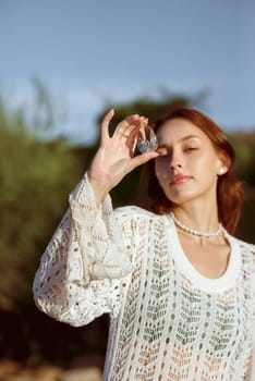 woman meditating on wild beach shore and holding crystal heart.close up of beautiful young girl on sea beach. she enjoys weather. near face holds crystal from crystal. concept of summer sea morning .