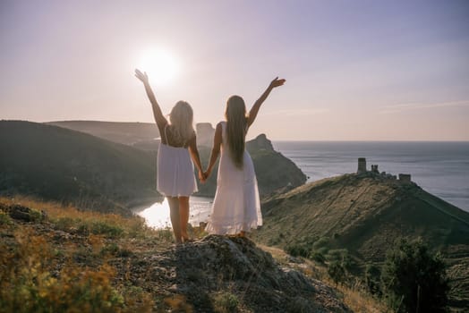 Two women are standing on a hill overlooking the ocean. They are holding hands and looking out at the water. The scene is peaceful and serene, with the sun shining brightly in the background