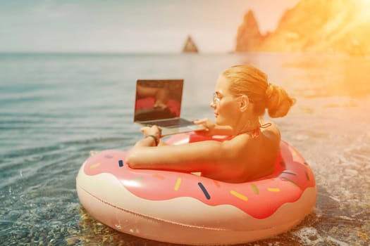 Woman laptop sea. Freelancer woman in sunglases floating on an inflatable big pink donut with a laptop in the sea. People summer vacation rest lifestyle concept