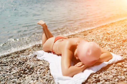 A woman sunbathes on the beach, lying on her stomach in a red swimsuit against the sea backdrop