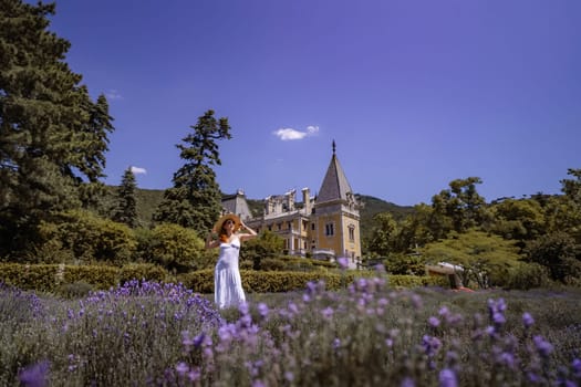 A woman is standing in a field of purple flowers. The sky is clear and the sun is shining brightly. The woman is wearing a white dress and a straw hat. The scene is peaceful and serene