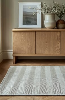 A stylish living room features a light rug, wooden cabinet, decorative vase, and a landscape picture, creating a warm and inviting atmosphere.