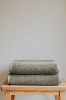 Soft green towels are neatly arranged on a wooden stool against a plain wall, creating a calm and minimalist atmosphere.