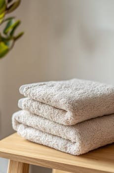 A neat stack of soft, light-colored towels rests on a simple wooden stool, enhancing the cozy atmosphere of a bathroom.