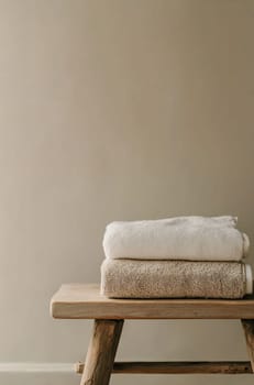 Two neatly stacked towels in neutral colors rest on a wooden stool against a simple beige wall, creating a calming atmosphere.